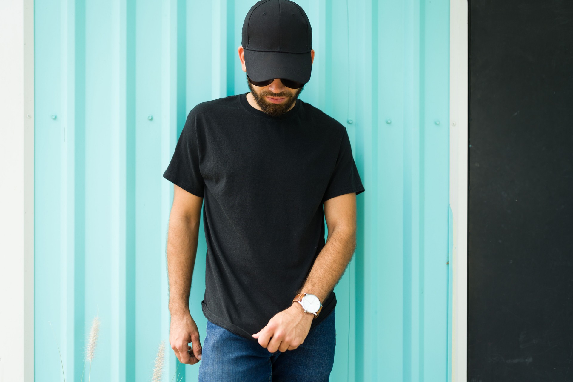 Mockup and casual wear design: hispanic man wearing a black t-shirt and cap against a turquoise background
